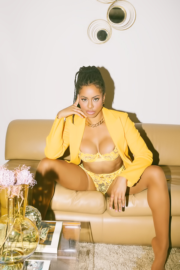 Kira Noir in lingerie posing on couch with plants and brick fireplace