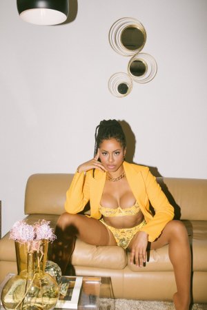 Kira Noir in lingerie posing on couch with plants and brick fireplace photo 3